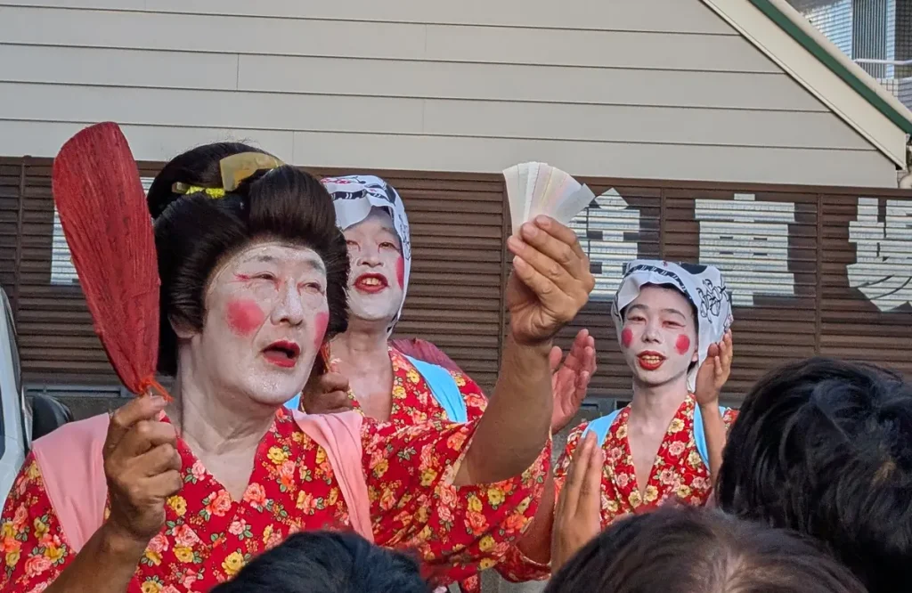 お札まきの踊り手たち。白粉を塗り赤い頬紅の女装姿で扇子やうちわを手に踊る