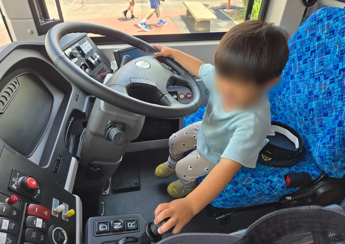江ノ電バスの運転席に座り、ハンドルを握って運転体験をする子ども