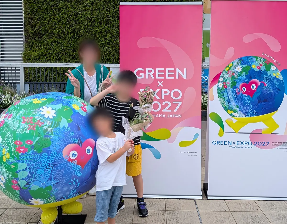 完成したミニブーケを持ってGREEN×EXPO 2027のバナーとトゥンクトゥンクの球体の前で記念撮影